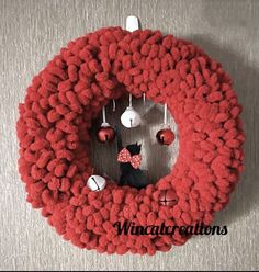 a red knitted wreath with a black cat in the center and ornaments hanging from it