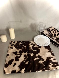 a cow print placemat, napkins and candle holders on a white table cloth