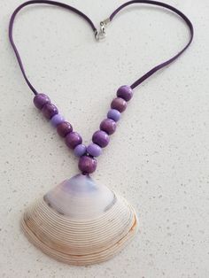 This necklace is handcrafted, featuring natural seashells adorned with vibrant purple beads. Bohemian Purple Necklace With Wooden Beads, Beach Jewelry With Colorful Purple Beads, Handmade Purple Beaded Necklaces For Beach, Purple Jewelry With Colorful Beads For Beach, Handmade Purple Beach Jewelry, Handmade Purple Beach Necklaces, Handmade Purple Necklaces For Beach, Beach Shell Necklace With Round Wooden Beads, Shell Necklace With Wooden Beads For Beach