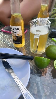 two bottles of beer sitting on top of a table next to limes and forks