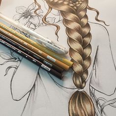 some pencils are laying on top of an art piece with a drawing of a woman's hair