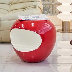 a red apple shaped ottoman sitting on top of a white tile floor next to a couch