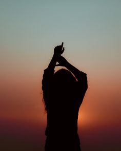 the silhouette of a woman with her hands up in the air at sunset or dawn