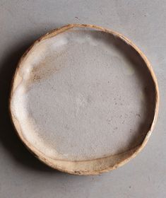 an empty wooden bowl sitting on top of a gray tablecloth covered floor with dirt