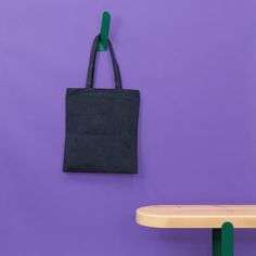 a black tote bag hanging on a purple wall next to a wooden table and bench