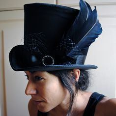 The Liza is a striking cabaret inspired full size top hat. It is covered with beautiful shiny black satin. It is decorated with black ribbon around the crown, black veil, half bow with black crystal buckle and two elegant black goose feathers. Also available as a medium size mini top hat: https://www.etsy.com/listing/256101614/victorian-witch-hatblack-mini-top?ref=shop_home_active_14 Need this TOP HAT in another color?Just send me a message to talk about a custom hat made just for you! This hat Carnival Adjustable Top Hat With High Crown, Adjustable High Crown Top Hat For Carnival, Gothic High Crown Costume Accessories For Costume Party, Gothic Wide Brim Party Hat, Black Brimmed Top Hat For Cosplay, Gothic Black Brimmed Costume Hat, Gothic High Crown Costume Hat For Cosplay, Black Gothic Hat For Costume, Black Gothic Hat For Cosplay