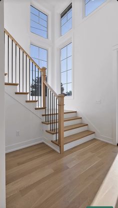 an empty room with wooden floors and white walls is pictured in this image, there are three windows on the second floor