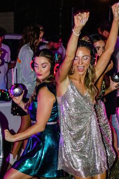 two women dancing at a party with headphones in their ears and other people behind them