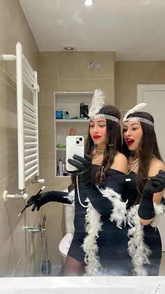 two women dressed in costumes taking a selfie in a bathroom mirror with their hands together