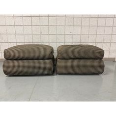 a pair of brown and white checkered fabric footstools in front of a tiled wall