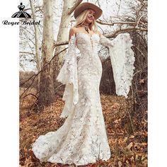 a woman in a white dress and hat standing next to trees with leaves on the ground