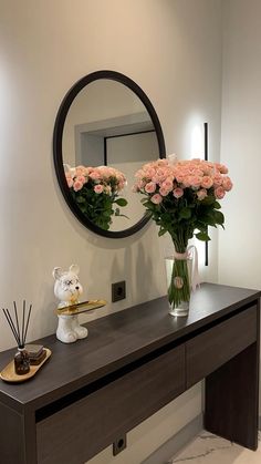 a vase with pink roses on a table in front of a mirror and candle holder