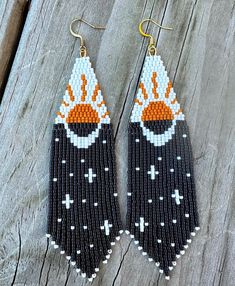 two pairs of beaded earrings with an orange and white design on them, sitting on a wooden surface