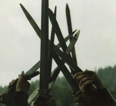 two hands holding up large knives in front of trees