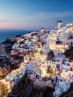 an aerial view of white buildings on the cliff by the ocean at night, with lights lit up