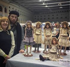 a man and woman standing next to a table with dolls on it