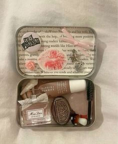 an open tin with various items in it on a white sheeted surface, including toothbrushes and soaps