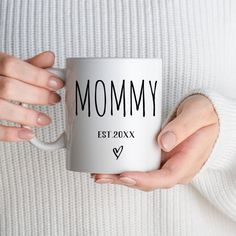 a woman holding a white coffee mug with the word mommy on it in front of her