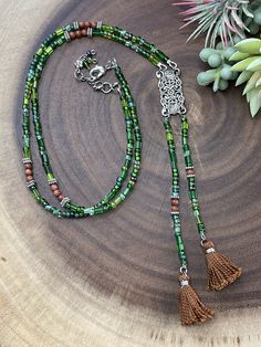 This gorgeous necklace with two tassels is designed with a unique look. It is made from a mix of czech glass beads in different shades of green and shapes. In between the purple beads are brown agate beads for a beautiful contrast. All metal components are silver plated. The pendant connector is vintage inspired rectangle shape that is about 1.25 inches long. The entire length of the pendant with tassels is 6.25 inches long. This necklace is similiar to a lariat style. The necklace length is 27. Adjustable Green Beaded Lariat Necklace, Adjustable Green Bohemian Lariat Necklace, Adjustable Green Jewelry With Tassels, Adjustable Green Beaded Tassel Necklace, Handmade Green Bohemian Lariat Necklace, Green Handmade Bohemian Lariat Necklace, Green Bohemian Handmade Lariat Necklace, Green Beaded Bohemian Tassel Necklace, Green Bohemian Beaded Tassel Necklace