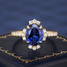 an oval shaped blue sapphire and diamond ring on top of a black velvet book with gold trimming