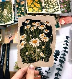 a person holding up a piece of paper with daisies on it in front of flowers