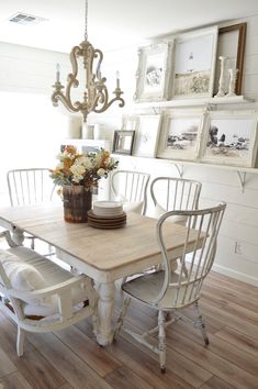 a dining room table with white chairs and pictures on the wall