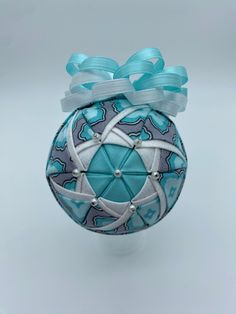 an ornament with blue and white designs on it, tied up to a ribbon