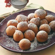 powdered sugar coated doughnuts on a plate with a cup of tea in the background