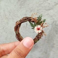 a hand holding a piece of wood with flowers on it and greenery in the middle