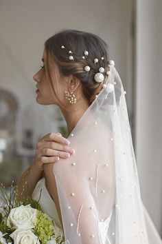 a woman wearing a veil and holding a bouquet in her hand with pearls on it