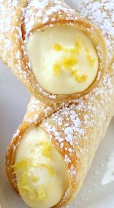 two pastries on a white plate covered in powdered sugar and lemon zest