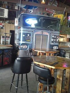 a large truck is parked in a garage next to tables and stools with chairs around them