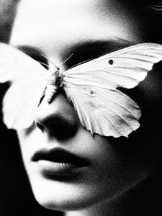 a black and white photo of a woman's face with a butterfly on her eye