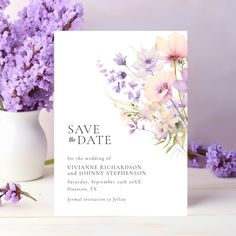 a white vase filled with purple flowers next to a save the date card on top of a table