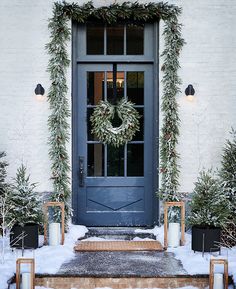 christmas wreaths and candles are on the front steps of a white building with snow