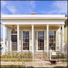 a small white house with columns on the front porch and a black cat walking in front