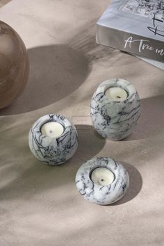 three marbled candles sitting on top of a table next to a book and vase