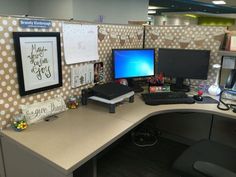 an office cubicle with two computer screens on it