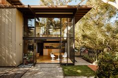 the entrance to a modern home with glass walls and doors on both sides, surrounded by trees