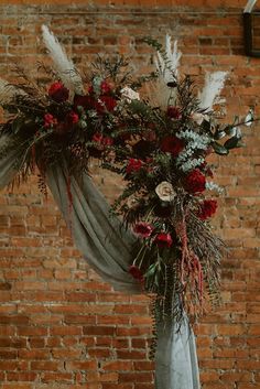 an arch decorated with flowers and greenery stands in front of a brick wall,