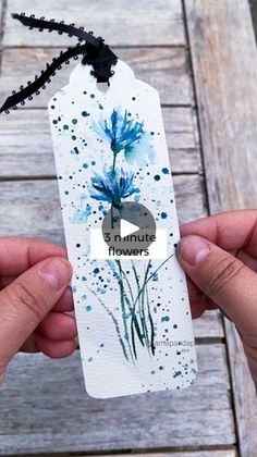 two hands holding an empty tag with blue flowers on it