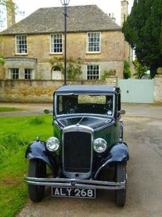 an old fashioned car parked in front of a large brick building on the side of a road