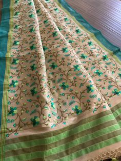 Gorgeous cotton tissue saree in soothing beige color. Colorful floral embroidery all over the saree is simply eye catching. Teal and light green border and anchal gives an elegant look. Comes with a separate blouse piece with saree border (7th pic). Suitable to wear in an afternoon party. Saree is 5.5+ yards and 43 inches wide Blouse piece is 31.5 inches Care: Dry clean only Disclaimer: Color and shade of saree may vary in the pictures than the actual item. There might be slight weaving irregula Pista Green Cotton Silk Saree With Resham Embroidery, Green Embroidered Cotton Silk Dupatta, Embroidered Beige Saree In Traditional Drape, Unstitched Green Saree With Floral Embroidery, Embroidered Cream Chanderi Saree, Traditional Embroidered Beige Saree, Green Traditional Dupatta With Floral Embroidery, Traditional Green Dupatta With Floral Embroidery, Floral Embroidery Cotton Silk Saree For Festivals