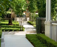 the walkway is lined with trimmed hedges and stone pillars, leading to an outdoor garden area