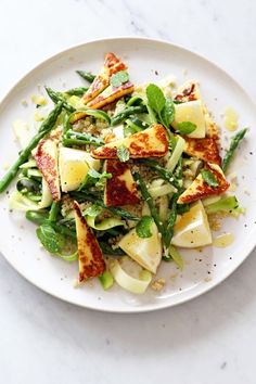 a white plate topped with green vegetables and tofu on top of a marble table