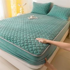 a person is pointing at a bed with blue sheets and pillows on top of it