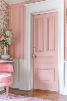 a pink room with floral wallpaper and an upholstered chair in front of the door