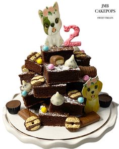 a white plate topped with lots of cakes and desserts covered in icing next to a cat figurine