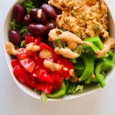 a white bowl filled with different types of vegetables and meat on top of lettuce