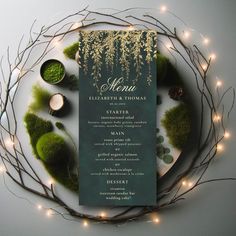 a green menu card surrounded by greenery and lite - up candles on a white plate